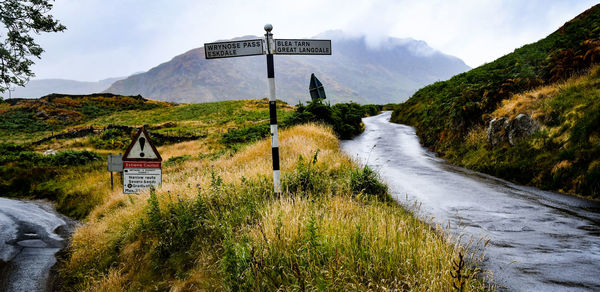 View of road sign by mountain against sky