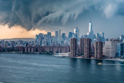 East river by modern buildings against cloudy sky at manhattan