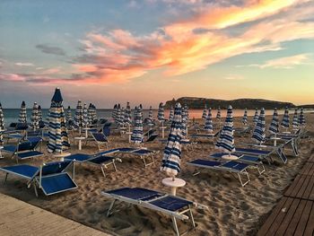 Empty chairs and tables at beach against sky during sunset