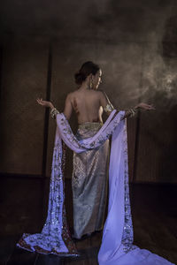 Rear view of topless mid adult woman wearing jewelries while standing against wall