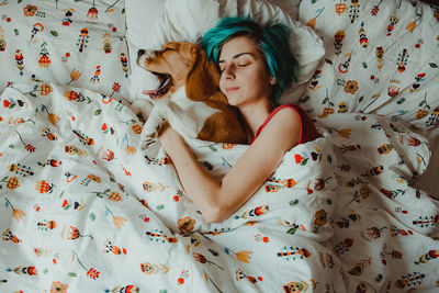 High angle view of woman sleeping with dog on bed