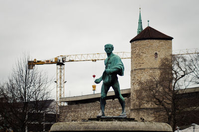 Low angle view of statue and old building against crane and sky