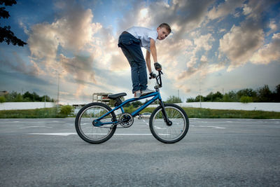 Man riding bicycle on road against cloudy sky