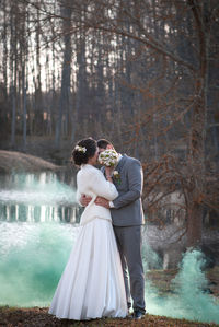 Newlywed couple kissing while standing against lake