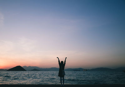 Woman with arms raised standing at sea shore against clear sky