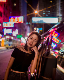 Portrait of smiling young woman standing against illuminated building