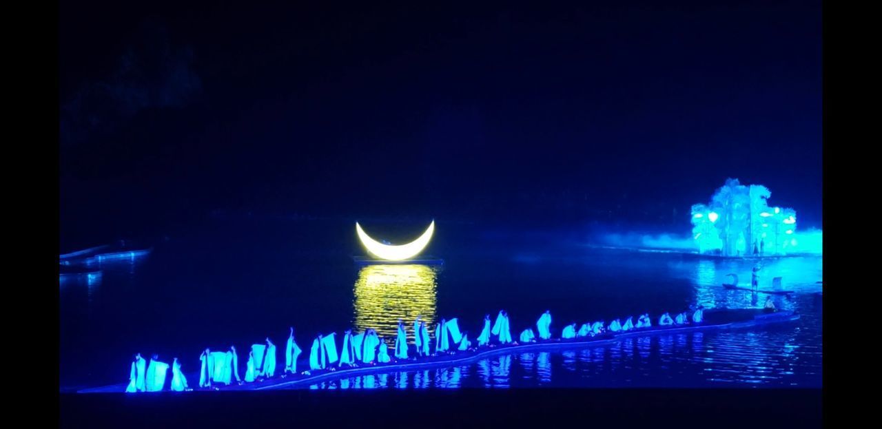 ILLUMINATED LIGHTS BY SEA AGAINST SKY IN CITY