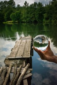 Cropped hand holding crystal ball with pier and lake reflection