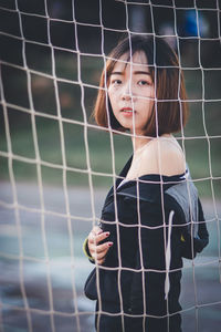 Portrait of beautiful young woman standing at goalpost