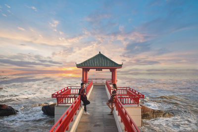 Couple standing on pier by sea during sunset