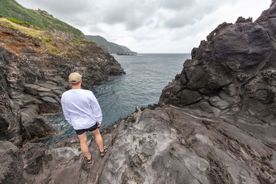 Rear view of man standing on rock by sea against sky