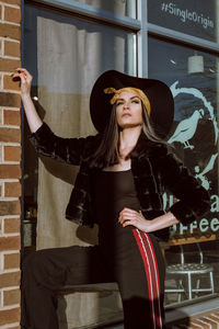 Young woman wearing hat standing against wall