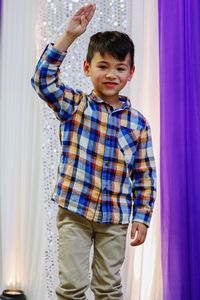 Portrait of boy with arms raised standing against curtain at event
