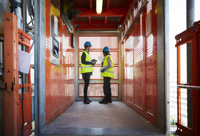 Full length of female engineers discussing while standing in freight elevator at construction site