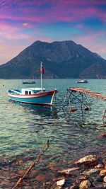 Boats moored on sea against mountains during sunset