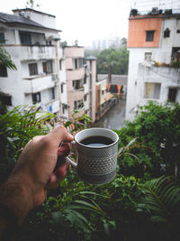 Cropped image of hand holding coffee cup against building