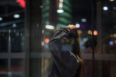Person standing by window in city at night