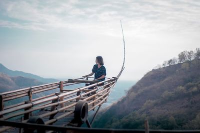 Woman sitting on wood at observation point against mountain and sky