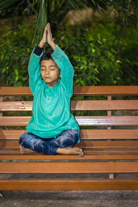 Young kid meditating at wood bench in traditional dress at evening from different angles