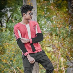 Young man looking away while standing on tree