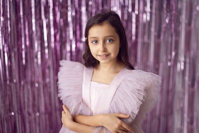 Beautiful girl with big eyes in a pink dress stands against the background of new year's tinsel