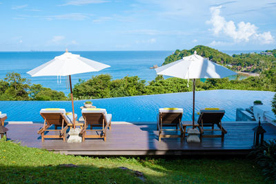 Empty chairs and tables and lounge chair at beach against sky