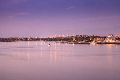 Illuminated buildings by sea against sky