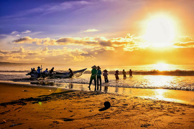 People on beach against sky during sunset