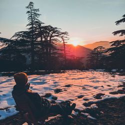 Man sitting on snowy looking at sunset