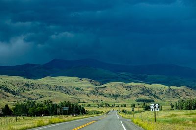 Country road amidst landscape against sky