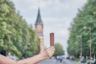 Senior woman's hand holding ice cream in chocolate over background of park and cathedral 