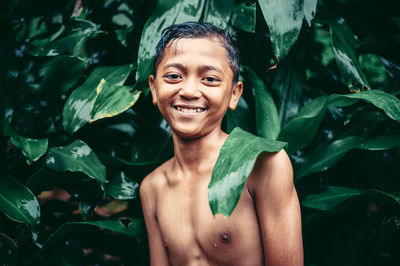 Portrait of smiling shirtless boy standing against plants