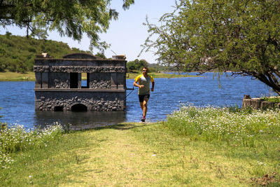 Rear view of man standing by lake against trees