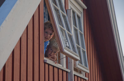 Portrait of brothers peeking through window of house