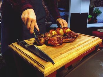 Midsection of person holding food with serving tongs on cutting board at home