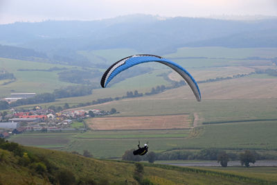 Person paragliding over landscape against sky