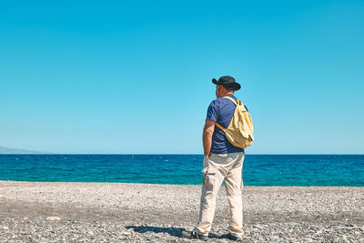 Back view of happy tourist man with backpack enjoying on the sea. wellness, success, freedom