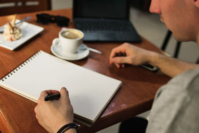 Crop freelancer drawing in notebook in cafe