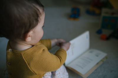 Side view of cute baby girl playing with book at home