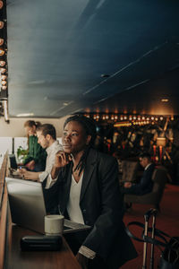 Thoughtful young businesswoman sitting with hand on chin in hotel lounge