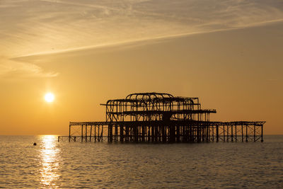 Silhouette crane by sea against sky during sunset