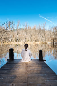 Rear view of girl sitting on pier over lake against sky