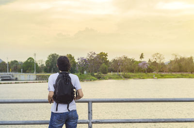 Rear view of man looking at river against sky