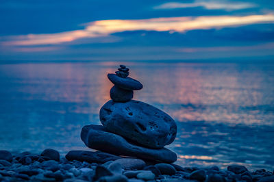 Stones on rocks at beach against sky during sunset