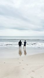 Rear view of friends standing at beach against sky