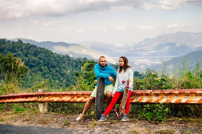 Couple sitting on railing against sky