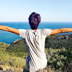 Woman with arms outstretched looking at sea