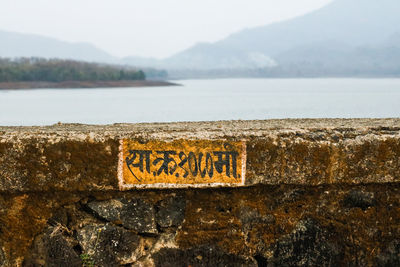 Close-up of text on retaining wall by sea against sky