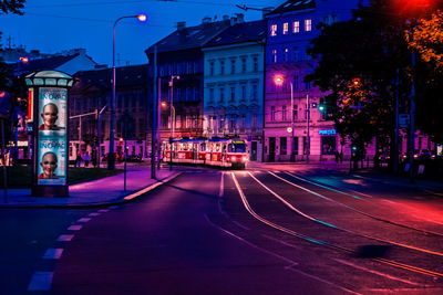 Illuminated city street by buildings at night