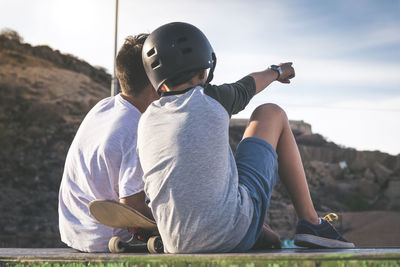 Rear view of boy sitting with friend on retaining wall